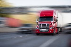 Bright red modern big rig semi truck with semi trailer move with cargo on the highway